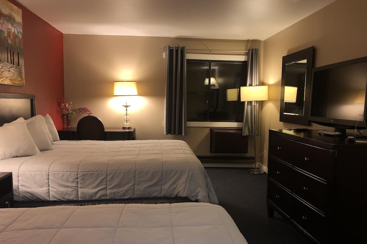 Une chambre d’hôtel avec deux lits, une télévision, une commode et une lampe.