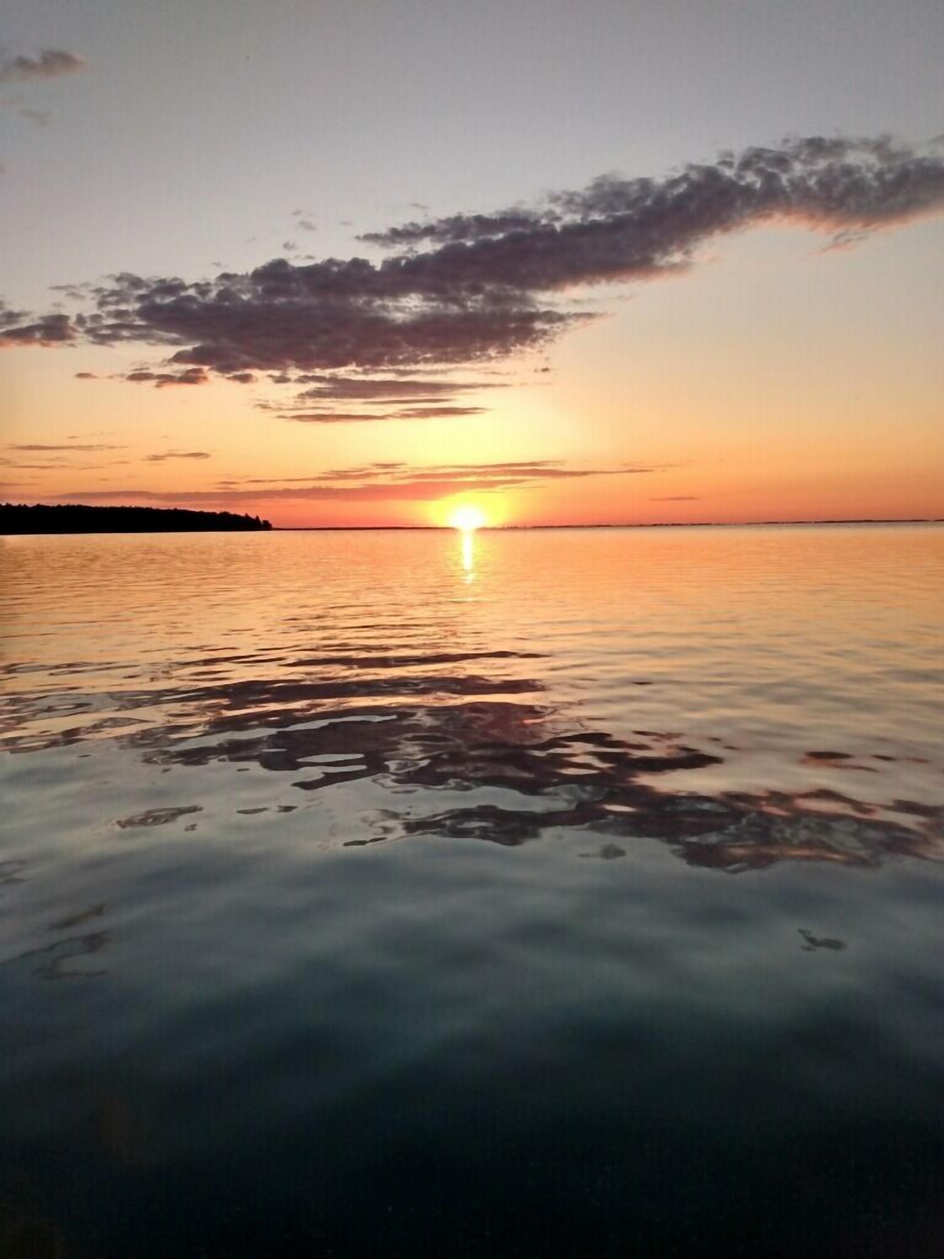 Un atardecer sobre una superficie acuática tranquila con la silueta de tierra en la distancia.
