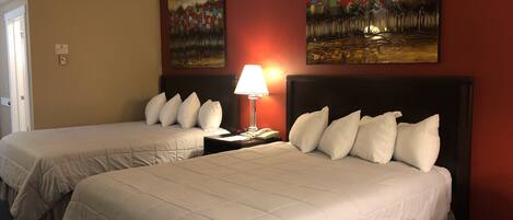 Een hotelkamer met twee bedden, een nachtkastje met een lamp en twee schilderijen aan de muur.