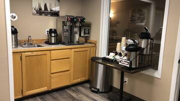 A compact kitchen with a coffee station, a sink, and wooden cabinets.