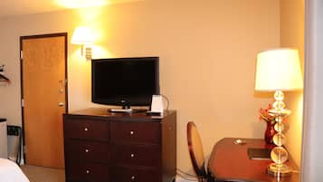 A hotel room with a wooden dresser, a flat-screen TV, a desk with a lamp, and a chair.