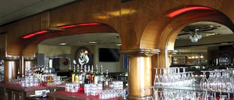A bar area with wooden arches, shelves of liquor bottles, and a variety of glassware.