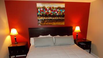 A neatly made bed with white bedding, two bedside tables with lamps, and a colorful abstract painting on the wall.