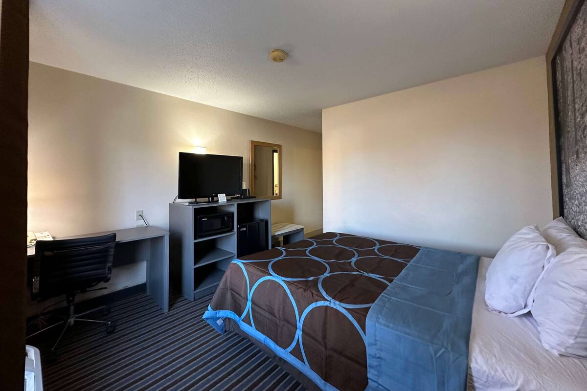 Ein Hotelzimmer mit einem Bett, einem Schreibtisch mit Stuhl, einem Fernseher und einem Kleiderschrank.