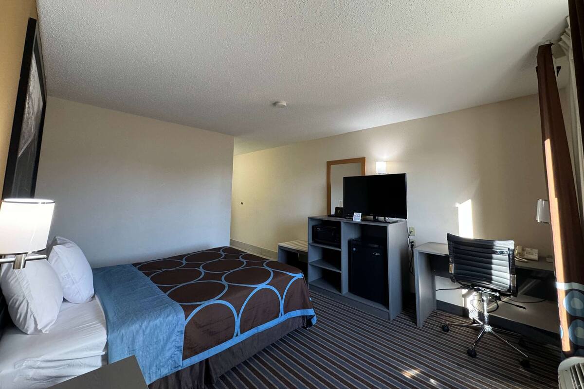 Ein Hotelzimmer mit einem Bett, einem Schreibtisch mit Computer, einem Fernseher und einem kleinen Kühlschrank.