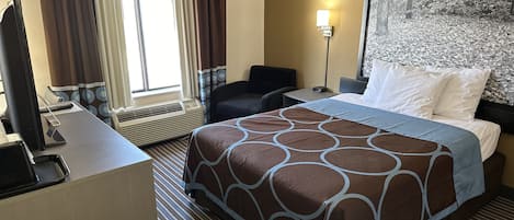 Une chambre d’hôtel avec un grand lit, un bureau avec un ordinateur, une chaise et une fenêtre avec des rideaux.