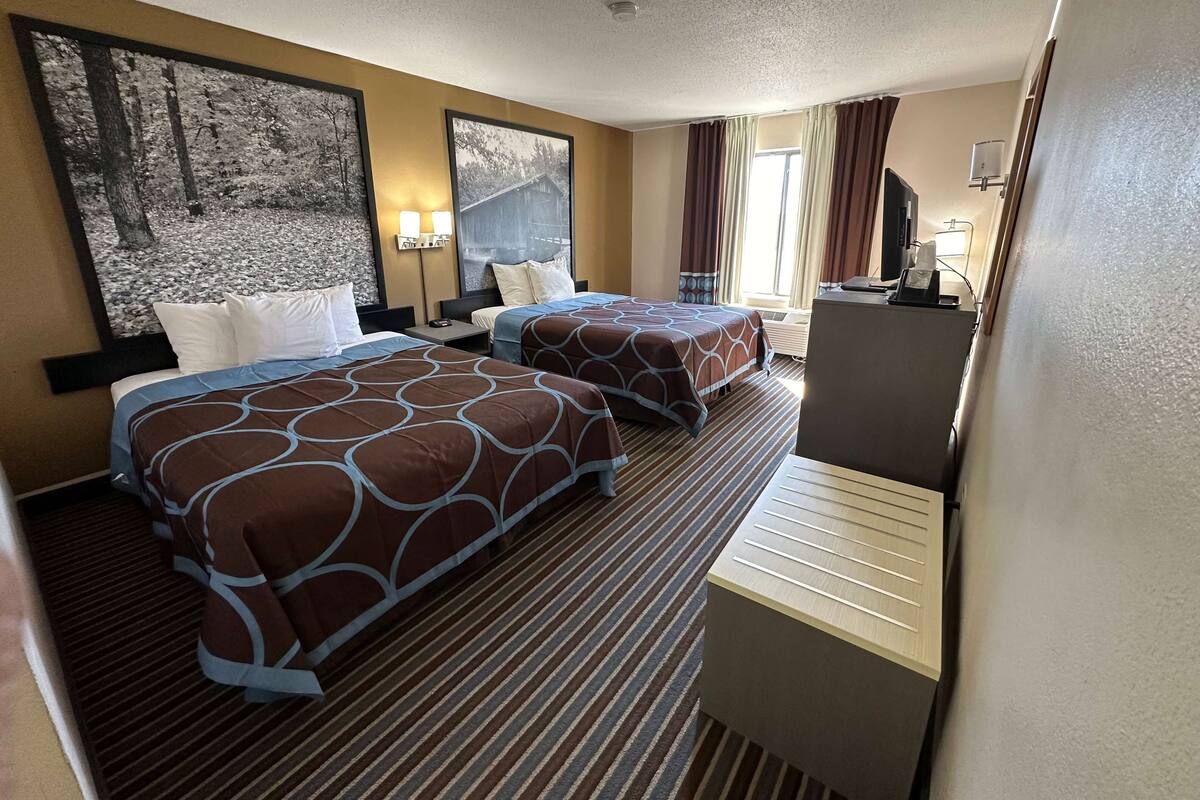 Ein Hotelzimmer mit zwei Betten, einem Schreibtisch, einem Fernseher und Bildern an den Wänden.