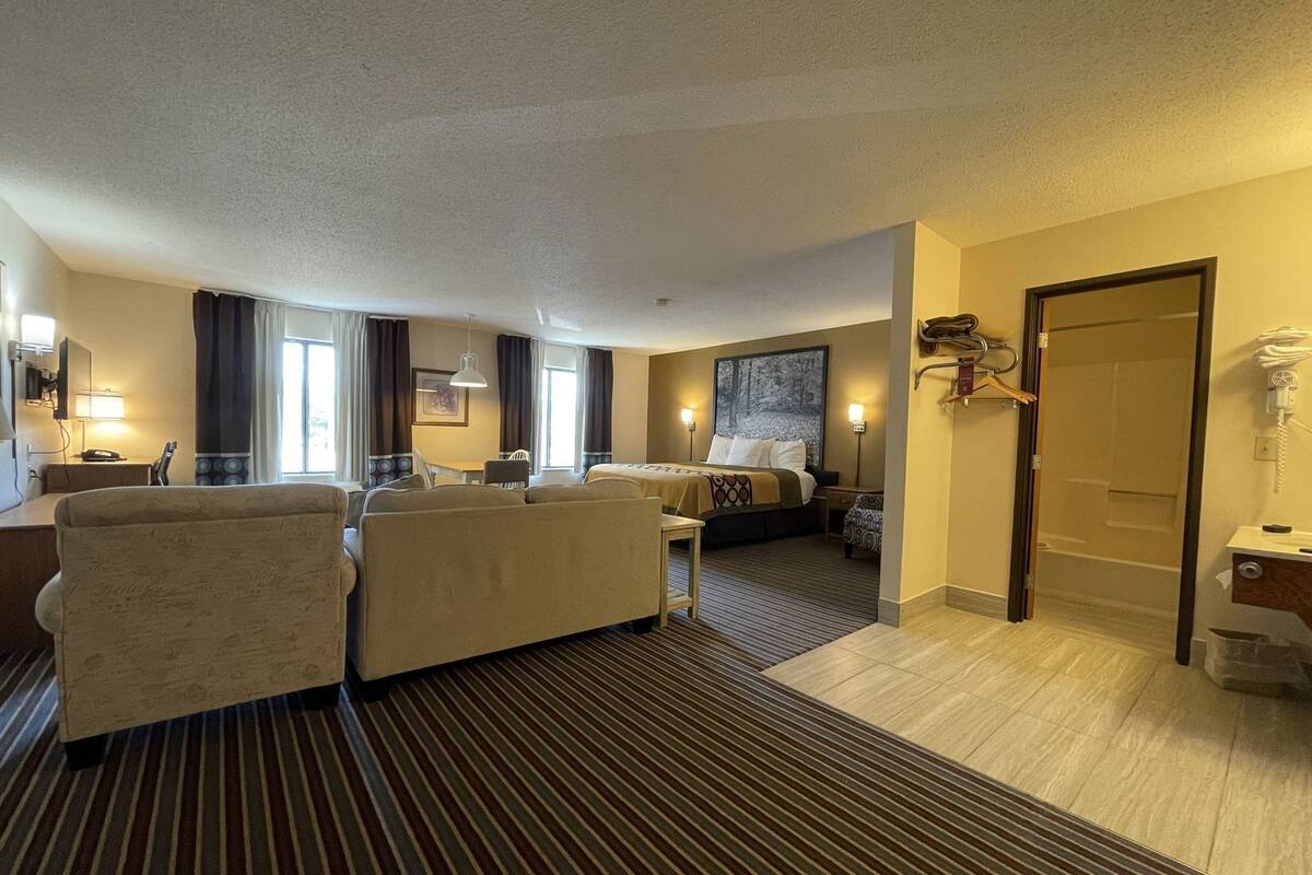Ein Hotelzimmer mit Bett, Sofa, Schreibtisch und Stuhl. Ein Fenster mit Vorhängen, ein Bild an der Wand und ein Telefon sind ebenfalls vorhanden.