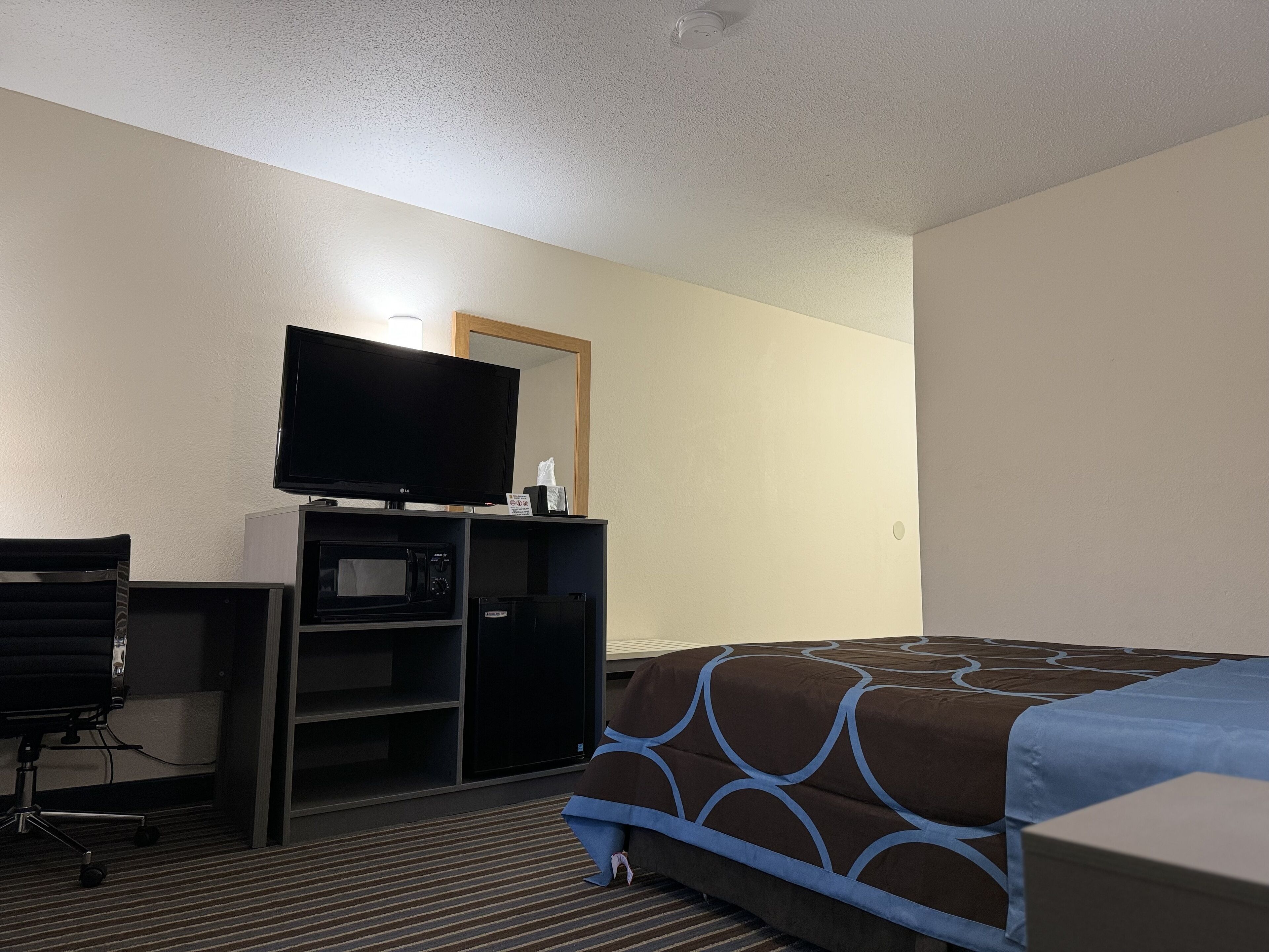 Ein Hotelzimmer mit einem Bett, einem Schreibtisch, einem Fernseher, einer Mikrowelle und einem Sessel.