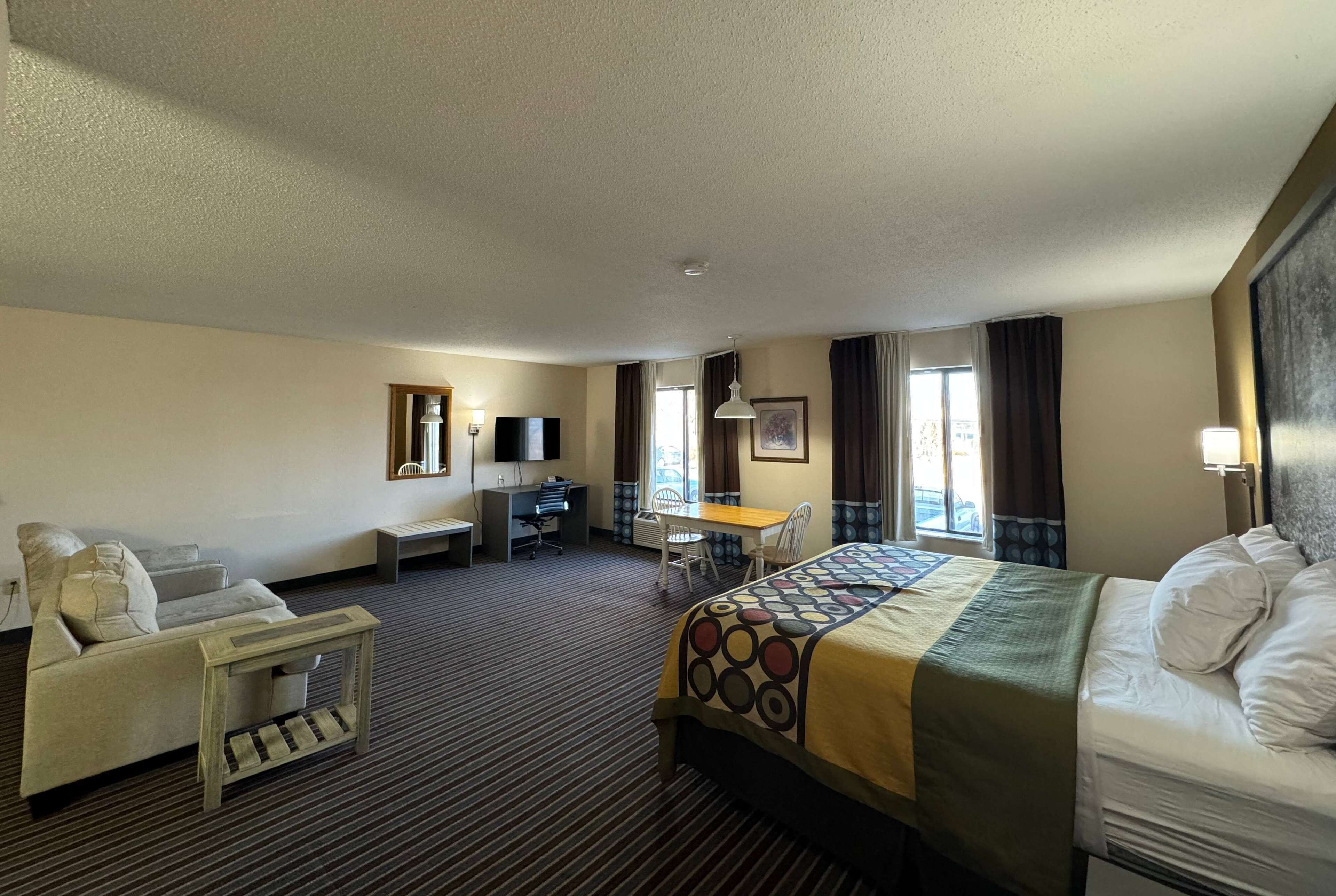 A hotel room with a bed, a desk, a chair, a sofa, and a TV.