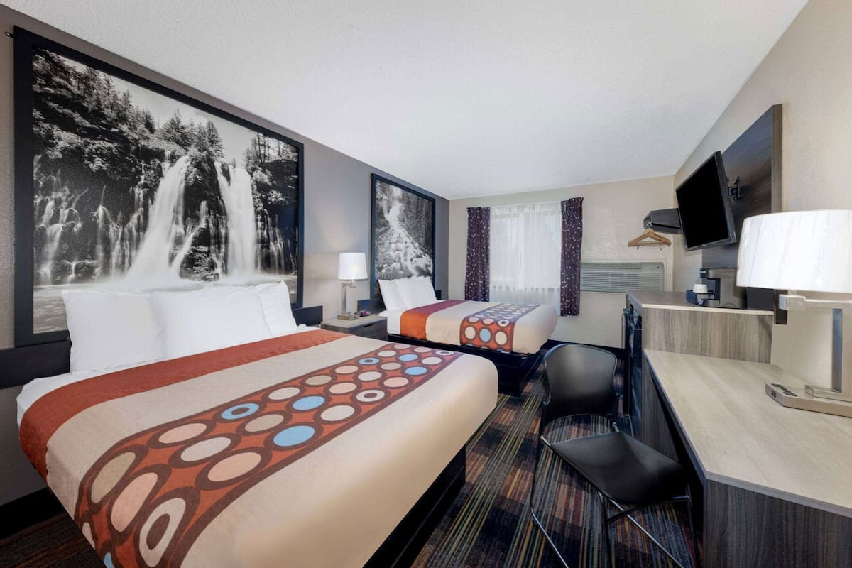 Une chambre d’hôtel avec deux lits, un bureau, une chaise, une télévision et une grande fenêtre avec des rideaux.