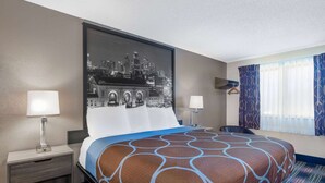 A hotel room with a large bed, two bedside tables with lamps, a cityscape artwork on the wall, and a window with patterned curtains. - Super 8 by Wyndham Kansas City at Barry Road/Airport (Kansas City)