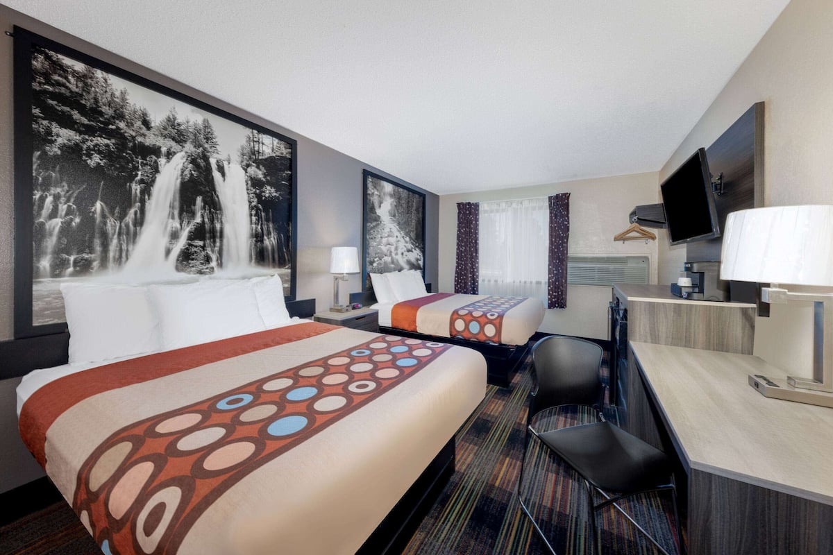 Une chambre d’hôtel avec deux lits, un bureau, une chaise, une télévision et un grand tableau représentant une cascade.