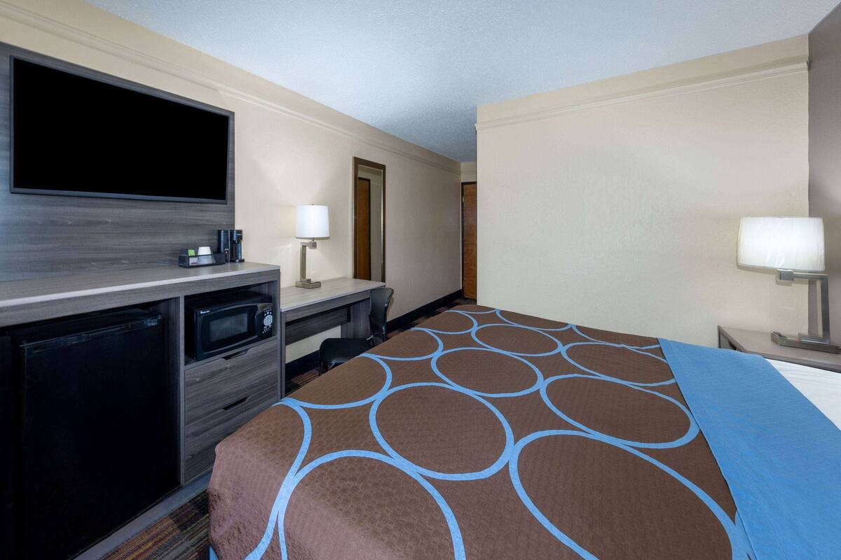 Une chambre d’hôtel équipée d’un téléviseur à écran plat, d’un bureau avec un ordinateur, d’un four à micro-ondes et d’une machine à café. La chambre comprend un lit recouvert d’une courtepointe aux motifs marron et bleu.