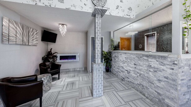 A modern lobby with a patterned floor, a reception desk, a mounted TV, and a decorative wall piece. - Super 8 by Wyndham Kansas City at Barry Road/Airport (Kansas City)