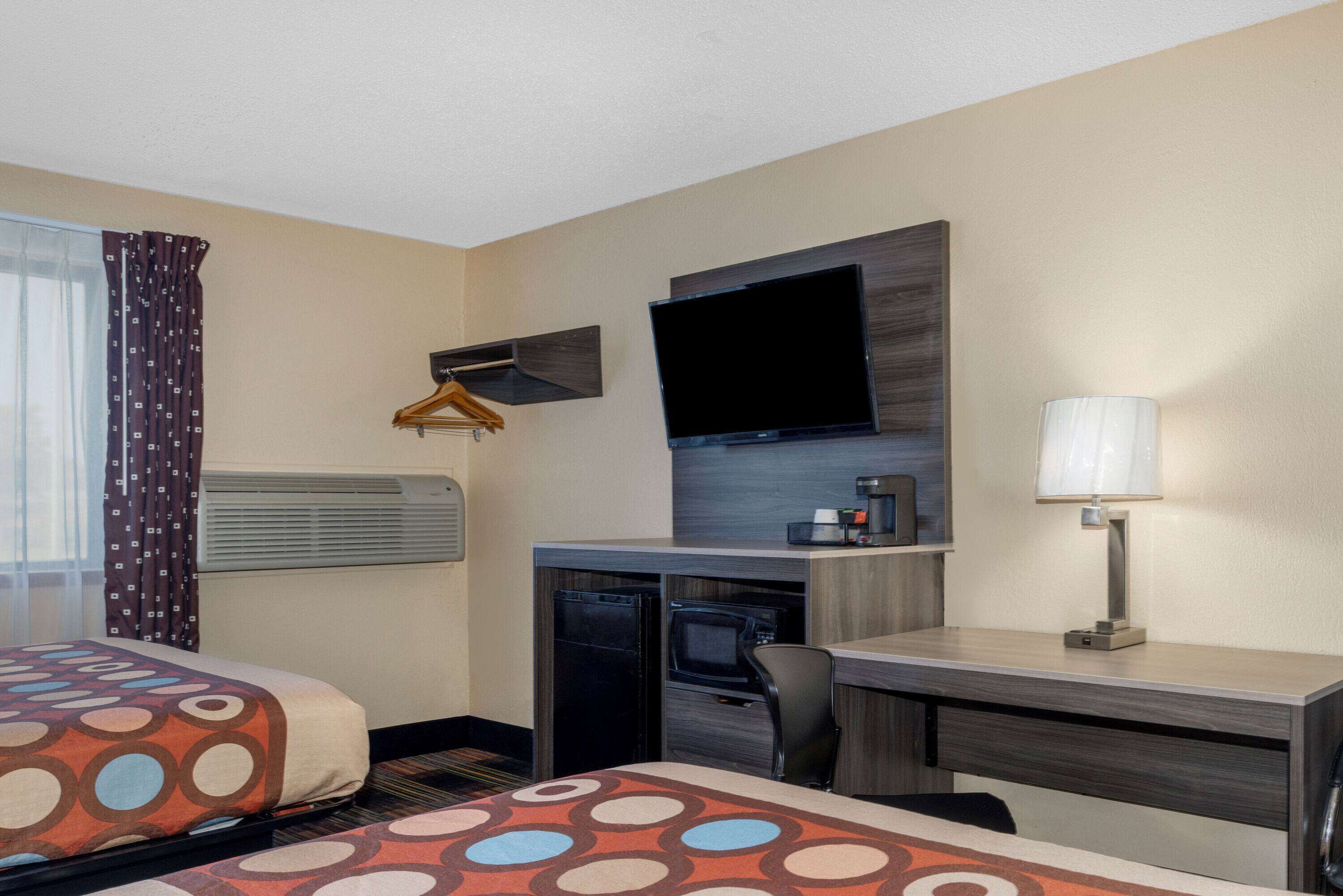 A hotel room with two beds, a desk, a television, a lamp, and a coffee maker.