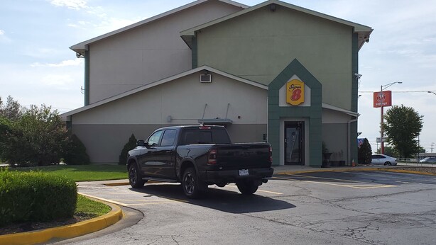 A black pickup truck parked in front of a building with a green and beige facade, a Super B Pop-Up sign, and a Super B sign. - Super 8 by Wyndham Kansas City at Barry Road/Airport (Kansas City)