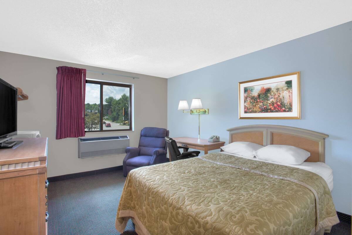 A hotel room with a bed, a desk, a chair, a TV, and a window with curtains.