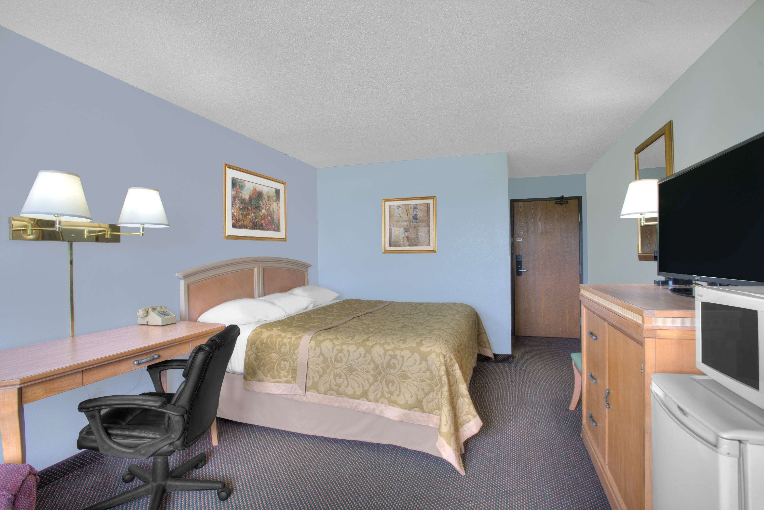 A hotel room with a bed, desk, chair, television, and a dresser.