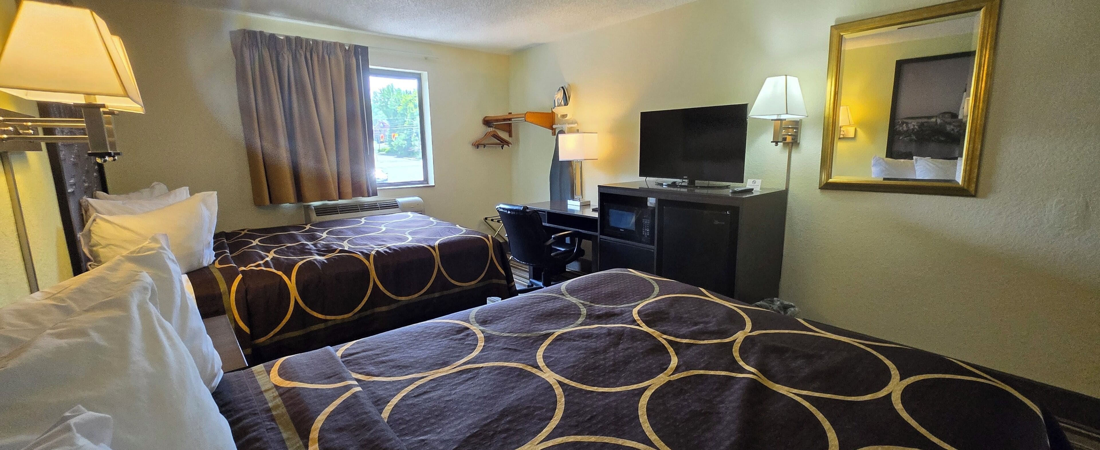 A hotel room with two beds, a desk with a TV, a lamp, and a window with curtains.