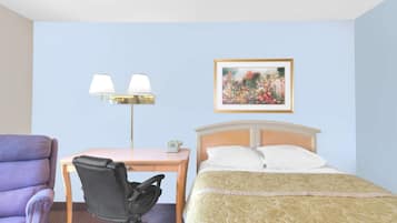 A hotel room with a bed, a desk with a chair, a lamp, and a framed picture on the wall.