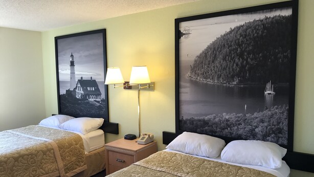 Ein Hotelzimmer mit zwei Betten, einem Nachttisch, einer Lampe und zwei gerahmten Bildern an der Wand.