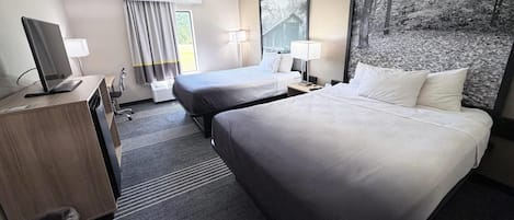 Une chambre d’hôtel avec deux lits, un bureau avec un ordinateur, une poubelle et une grande fenêtre avec des rideaux.