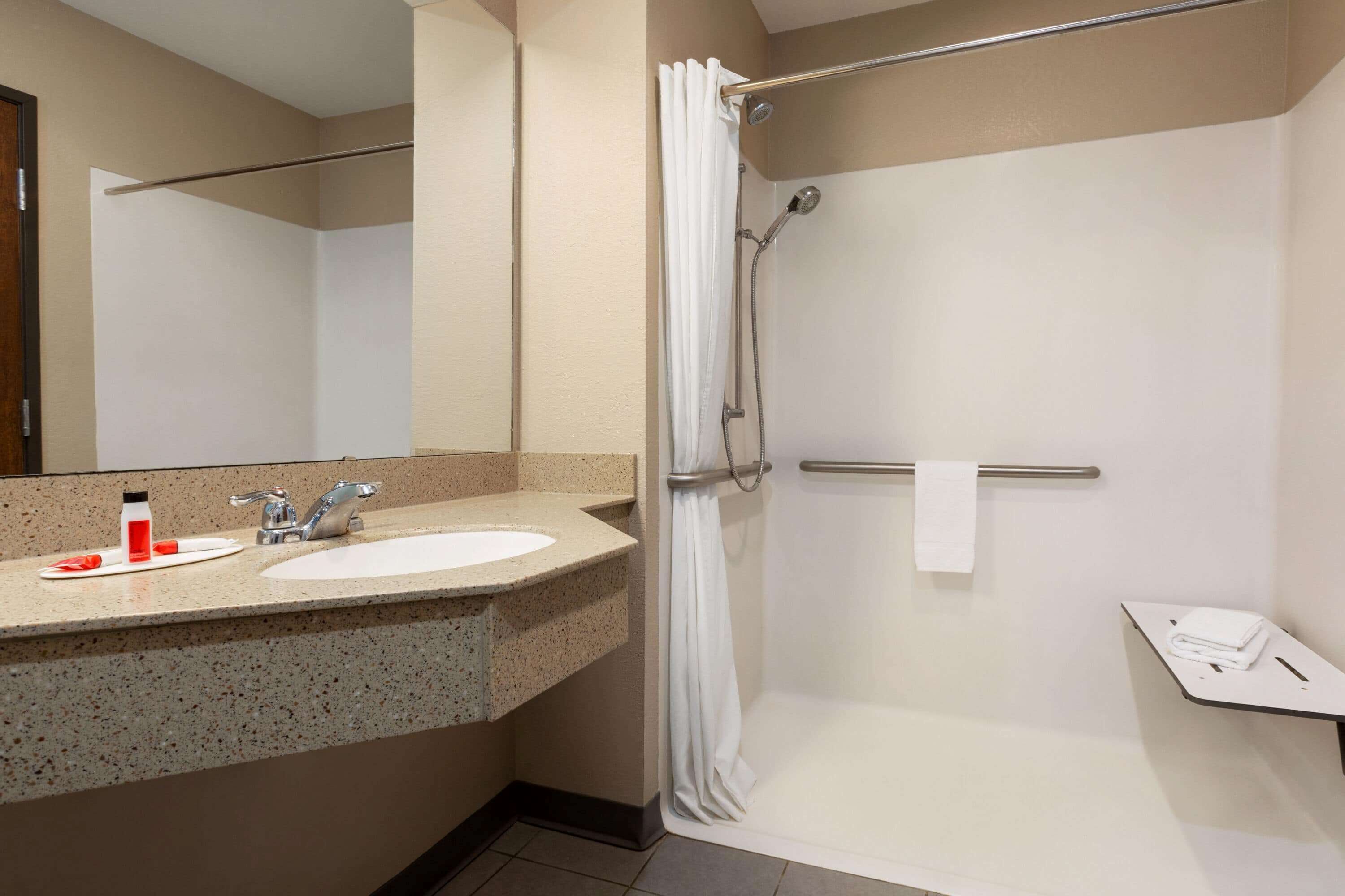 Un baño con lavamanos, espejo, ducha y perchero para toallas.