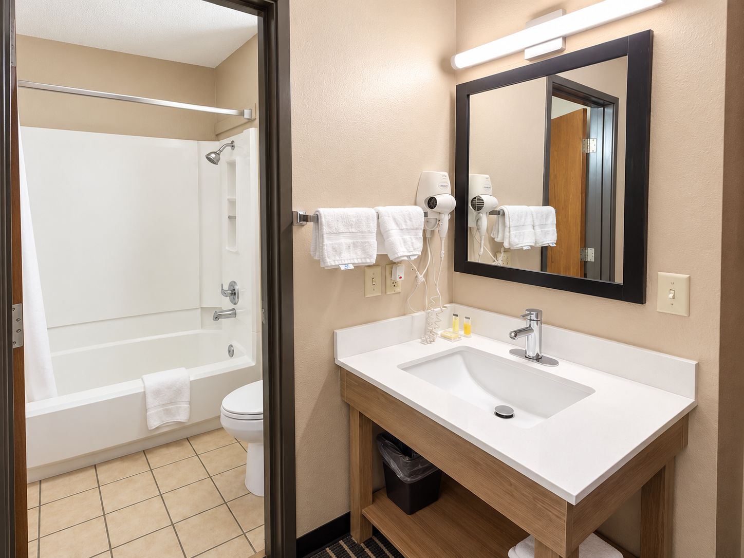 A bathroom with a bathtub, toilet, sink, and hair dryers.