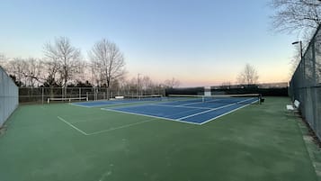 An outdoor tennis court with a net, surrounded by a fence and benches.
