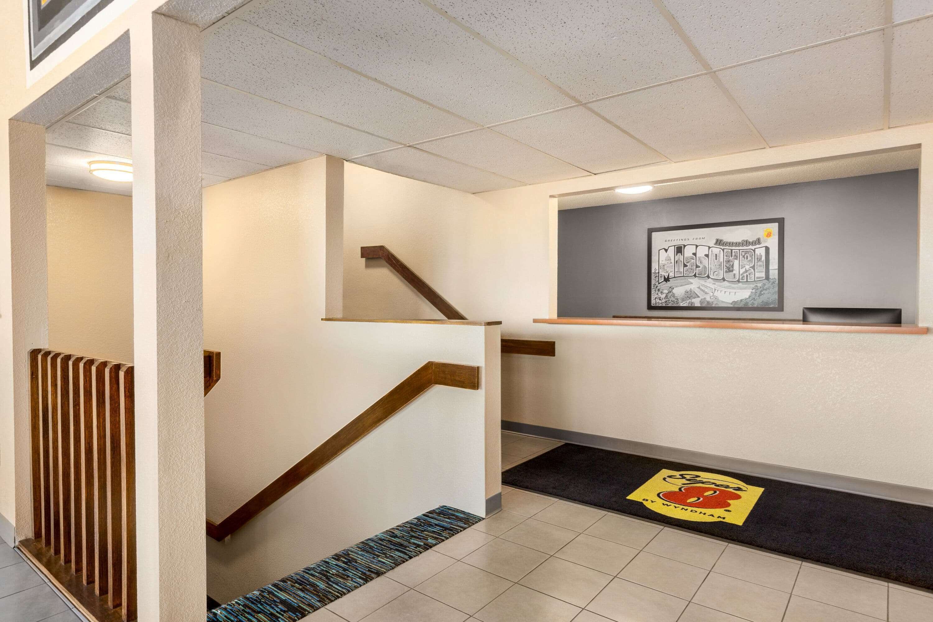 A hotel lobby with a staircase, a reception desk, and a framed welcome sign.