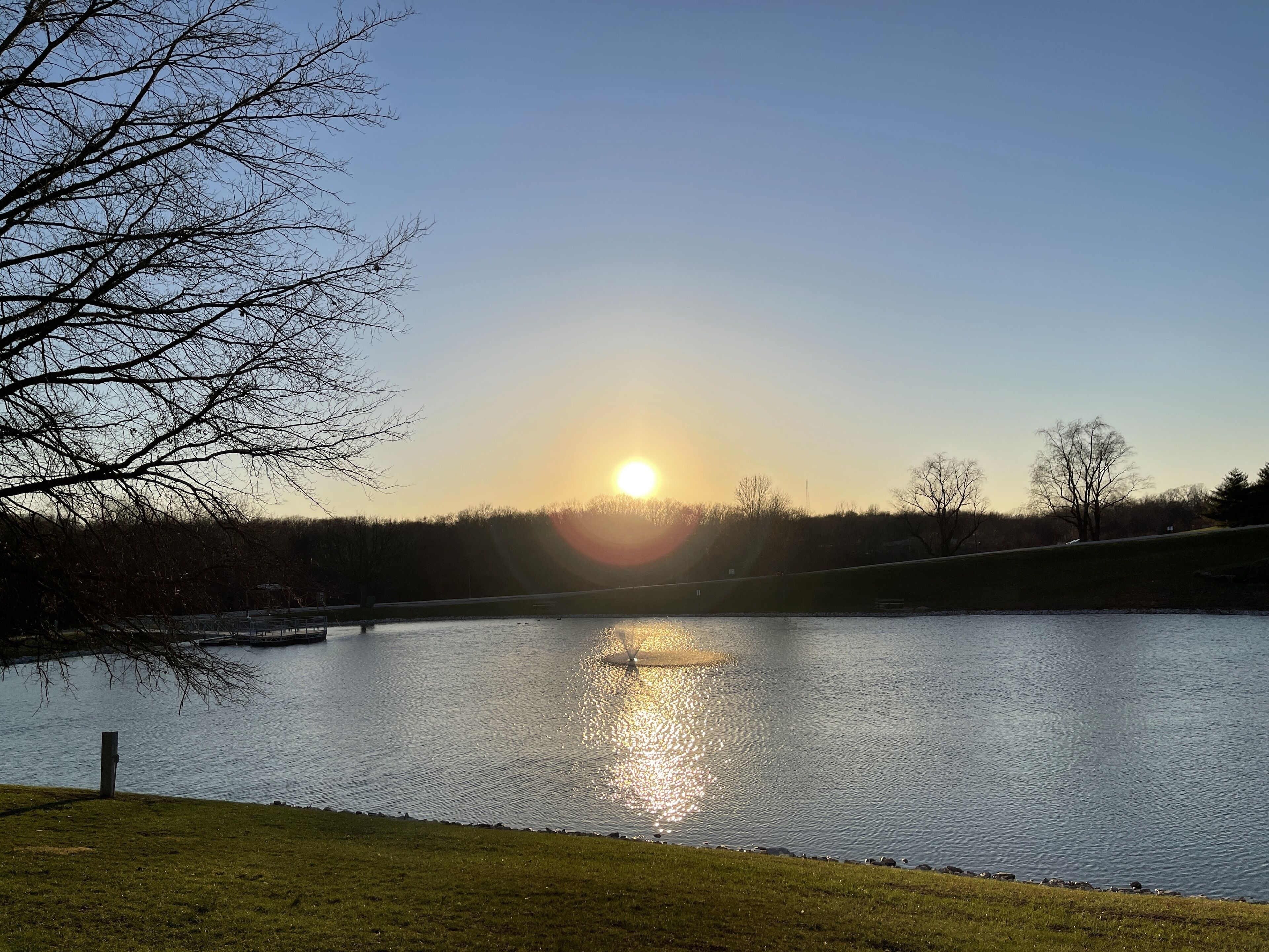 Una vista serena de un lago con cielo despejado y el sol poniéndose en el horizonte.