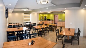 A dining area with multiple tables and chairs, a kitchen area with green walls, and a pink door. - Super 8 by Wyndham Branson/Andy Williams Theater (Branson)