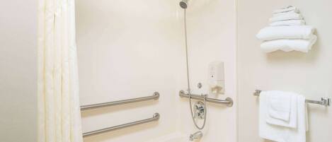 A bathroom with a shower, grab bars, a towel rack, and a toilet paper holder.