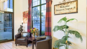 A lobby with two leather armchairs, a table with a vase of flowers, a large potted plant, and a welcome sign. - Super 8 by Wyndham Branson/Andy Williams Theater (Branson)
