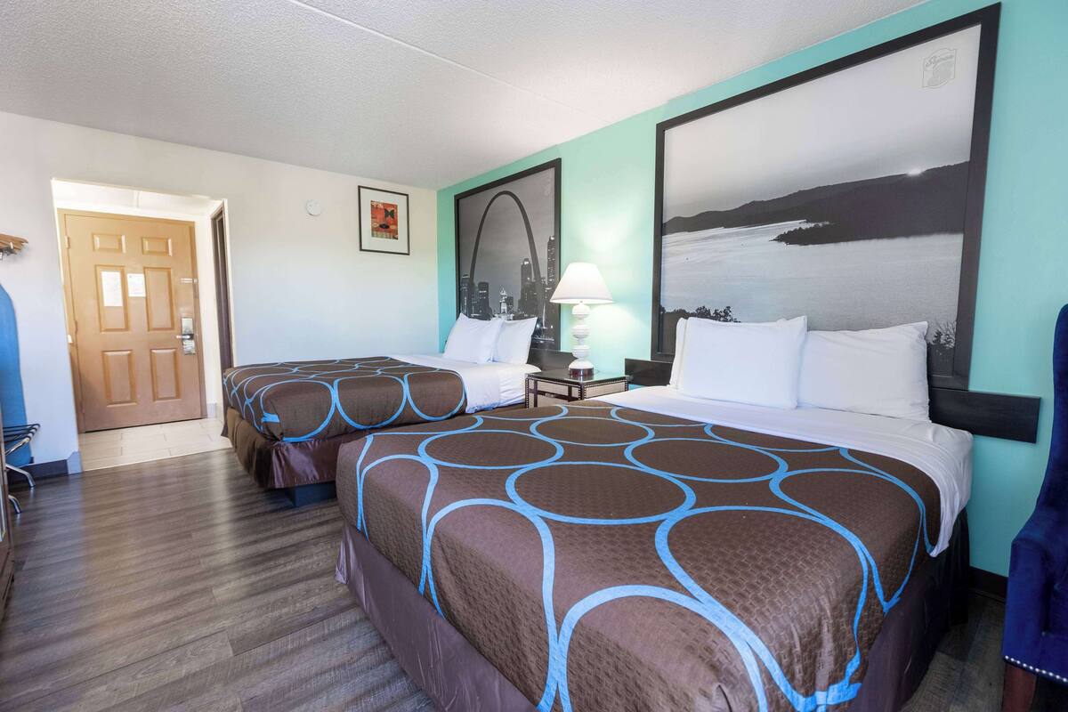 Habitación de hotel con dos camas, un cuadro de paisaje urbano y una lámpara.