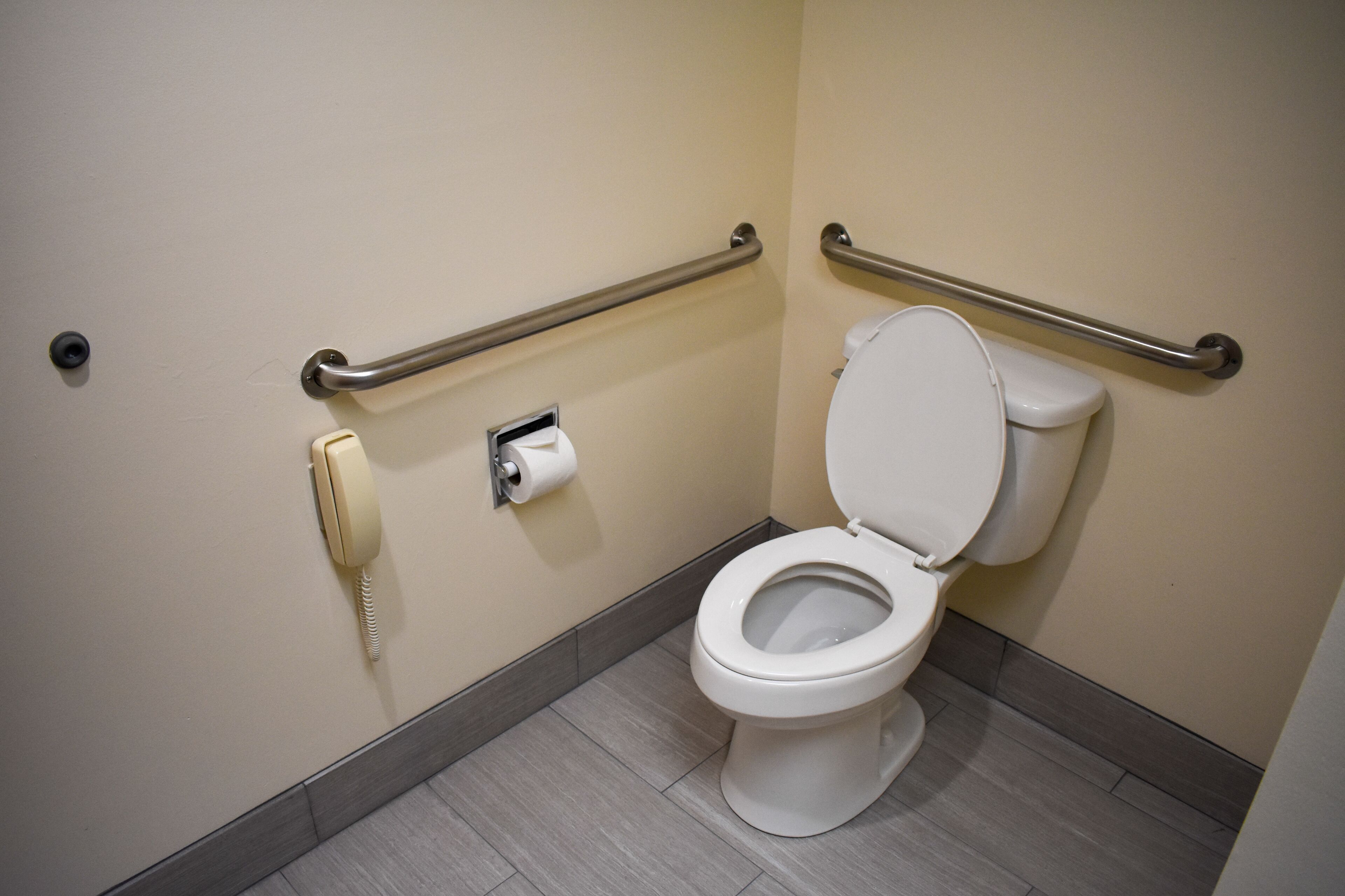 Un baño accesible para personas con movilidad reducida, con inodoro, barras de apoyo y teléfono.