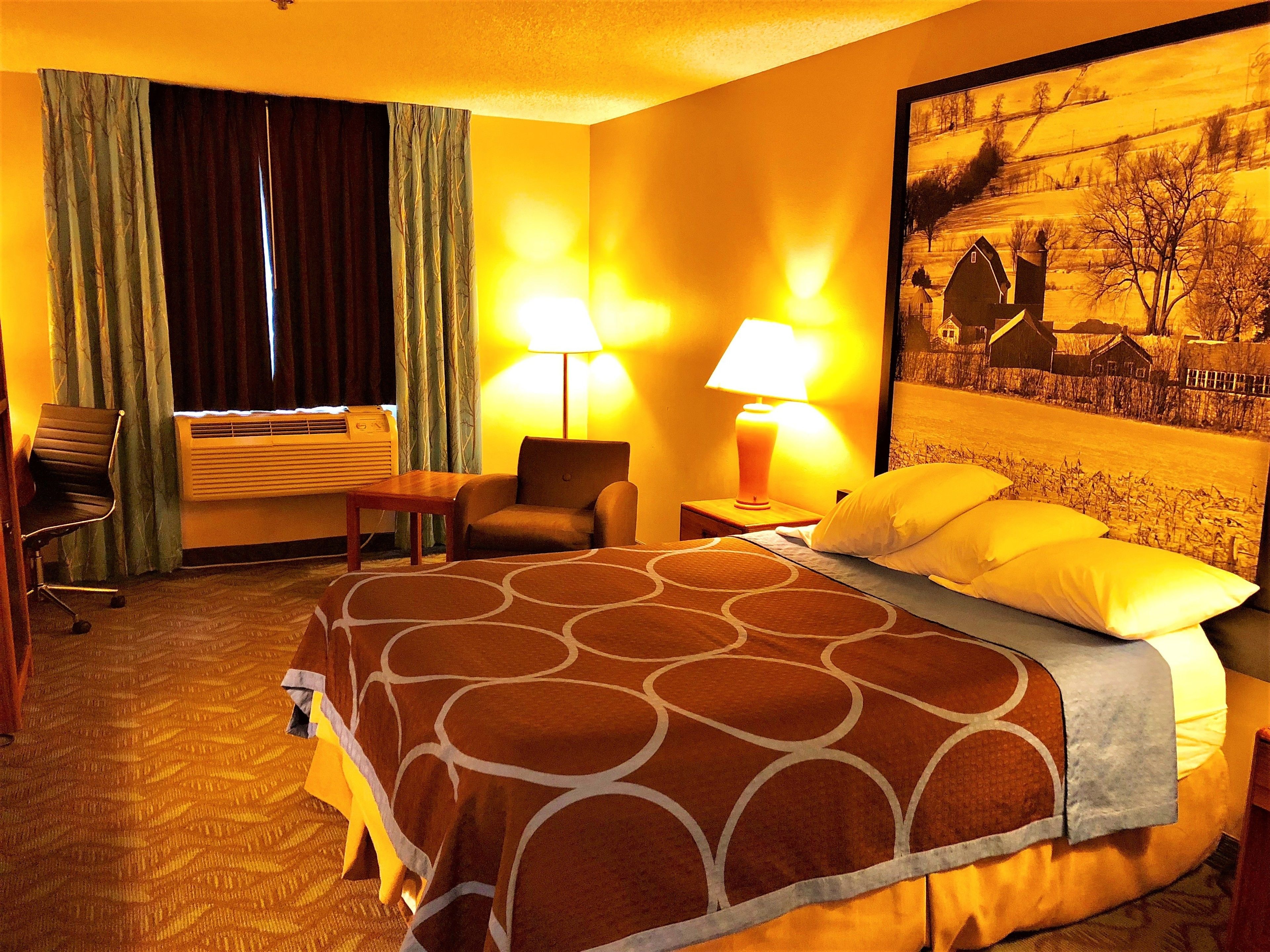 A hotel room with a large bed, two bedside lamps, a chair, a desk, and a window with curtains.