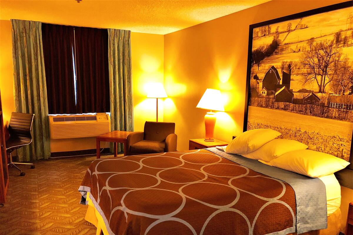 A hotel room with a large bed, two bedside lamps, a chair, a desk, and a window with curtains.