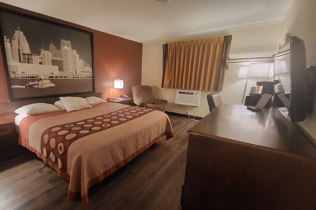 A hotel room with a large bed, two bedside tables with lamps, a desk with a chair, a large painting on the wall, and a window with curtains.