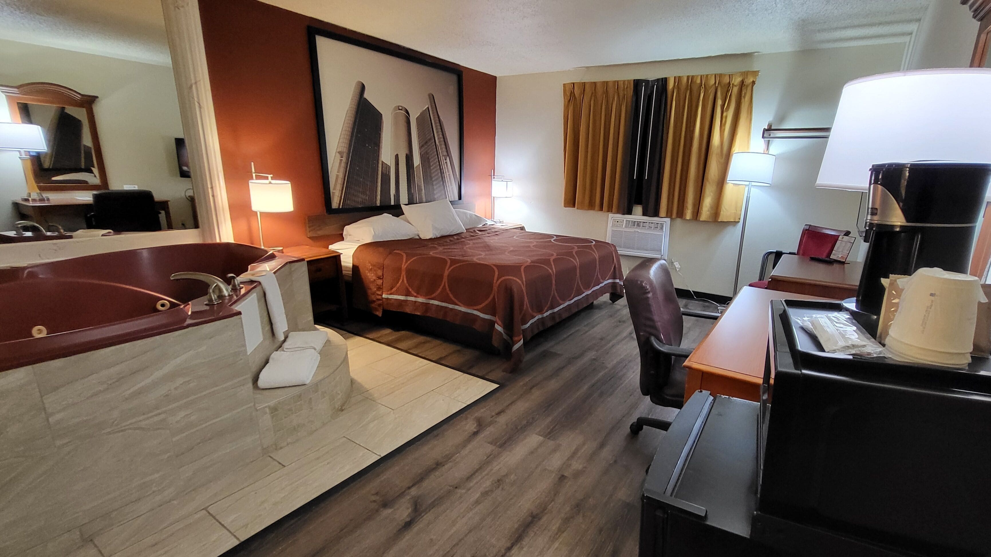 A hotel room with a large bathtub, two beds, a desk with a coffee maker, and a painting on the wall.