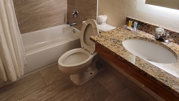 A bathroom with a bathtub, toilet, and granite countertop sink.
