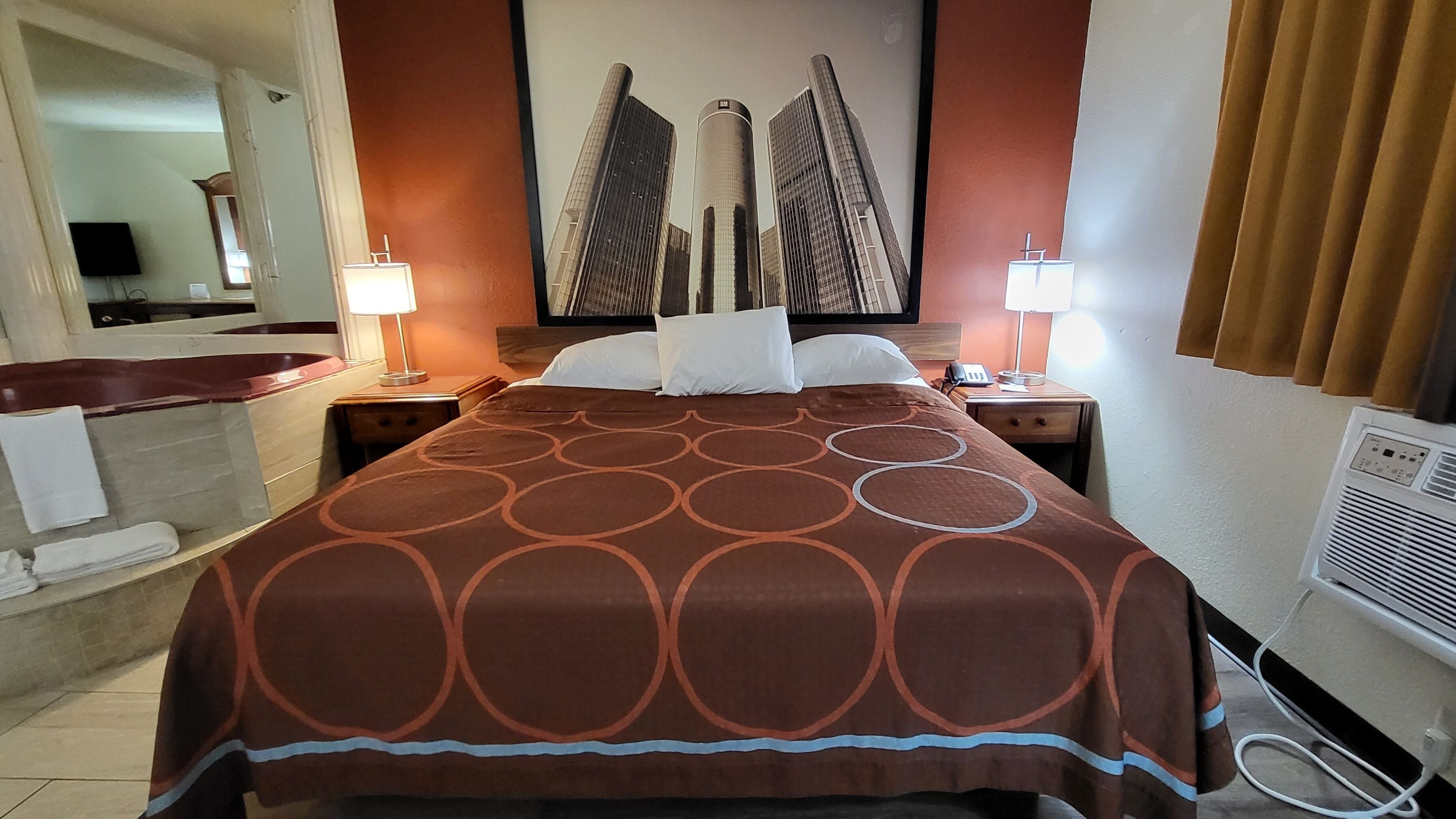 Habitación de hotel con una cama grande, dos mesitas de noche con lámparas, un baño con bañera y un cuadro grande en la pared.
