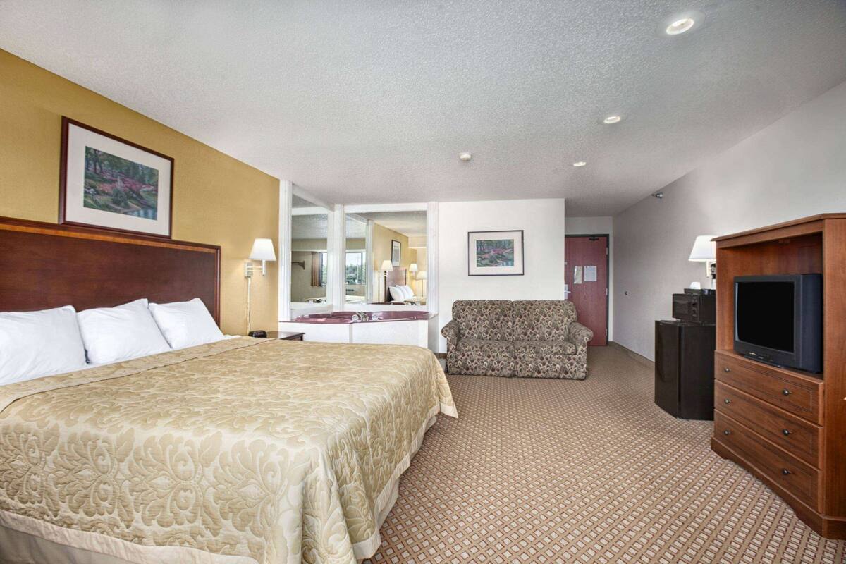 A hotel room with a large bed, a sofa, a television, and a desk with a mirror.