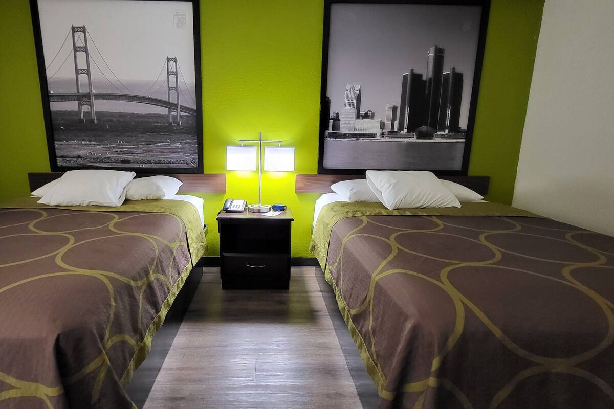 A hotel room with two beds, green walls, and two framed pictures of bridges.