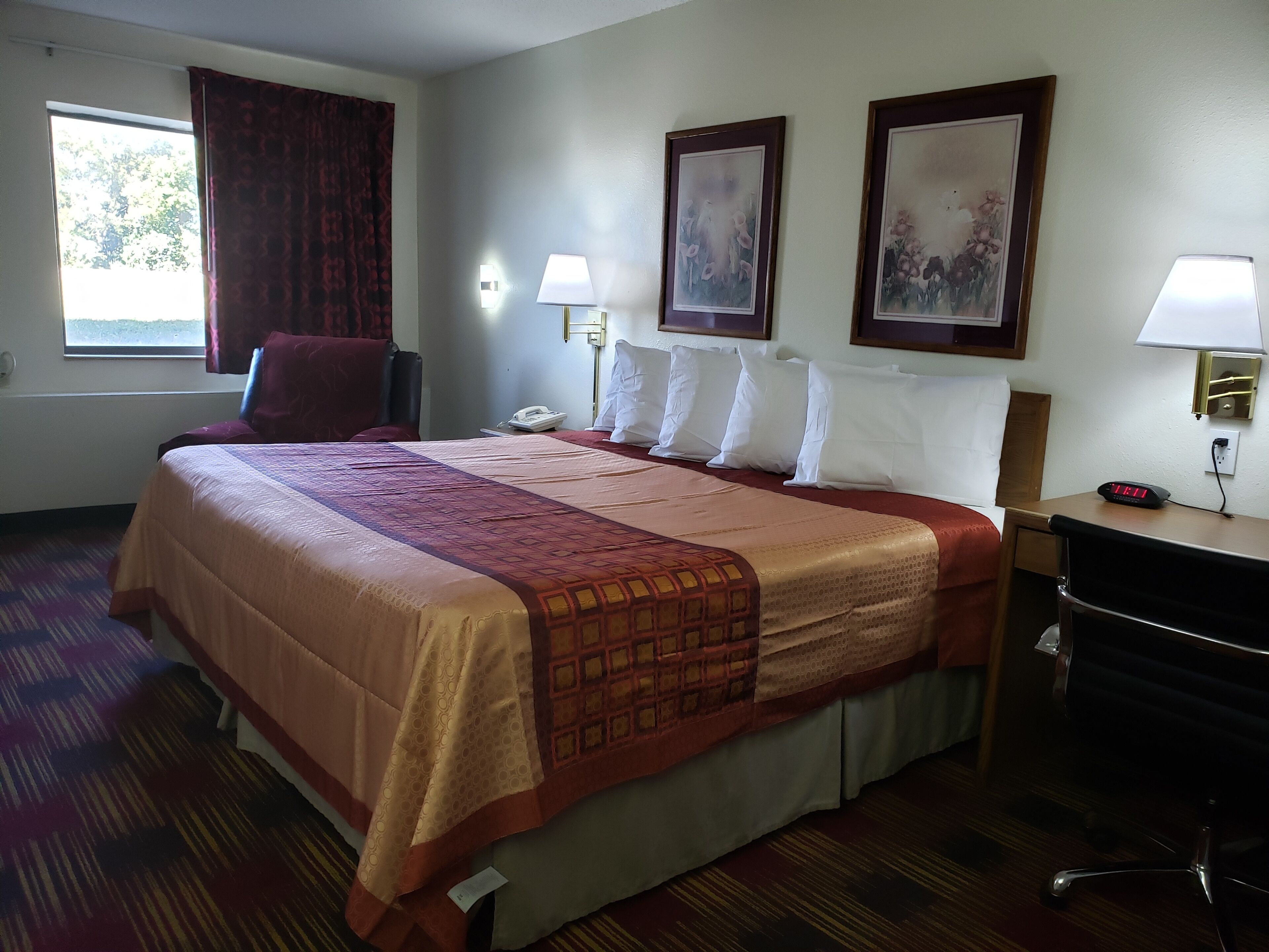 A hotel room with a large bed, a desk, a chair, a phone, and two wall-mounted lamps.