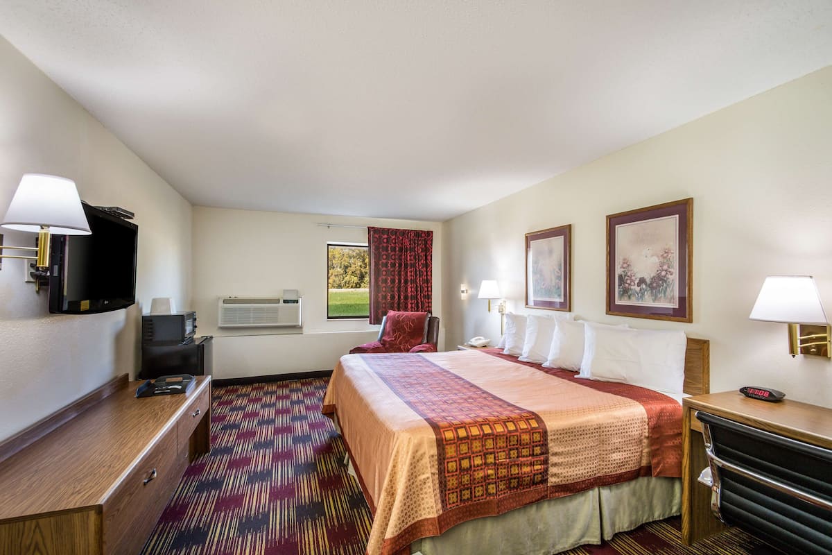 A hotel room with a bed, a desk, a chair, a television, and a window with curtains.
