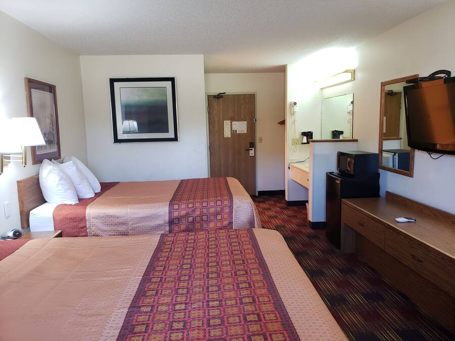 Hotellihuone, jossa on kaksi sänkyä, työpöytä, lipasto, peili, televisio ja ovi, joka johtaa toiseen huoneeseen.