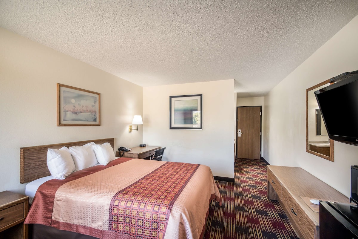 A hotel room with a large bed, a desk with a lamp, a television, and a carpeted floor.