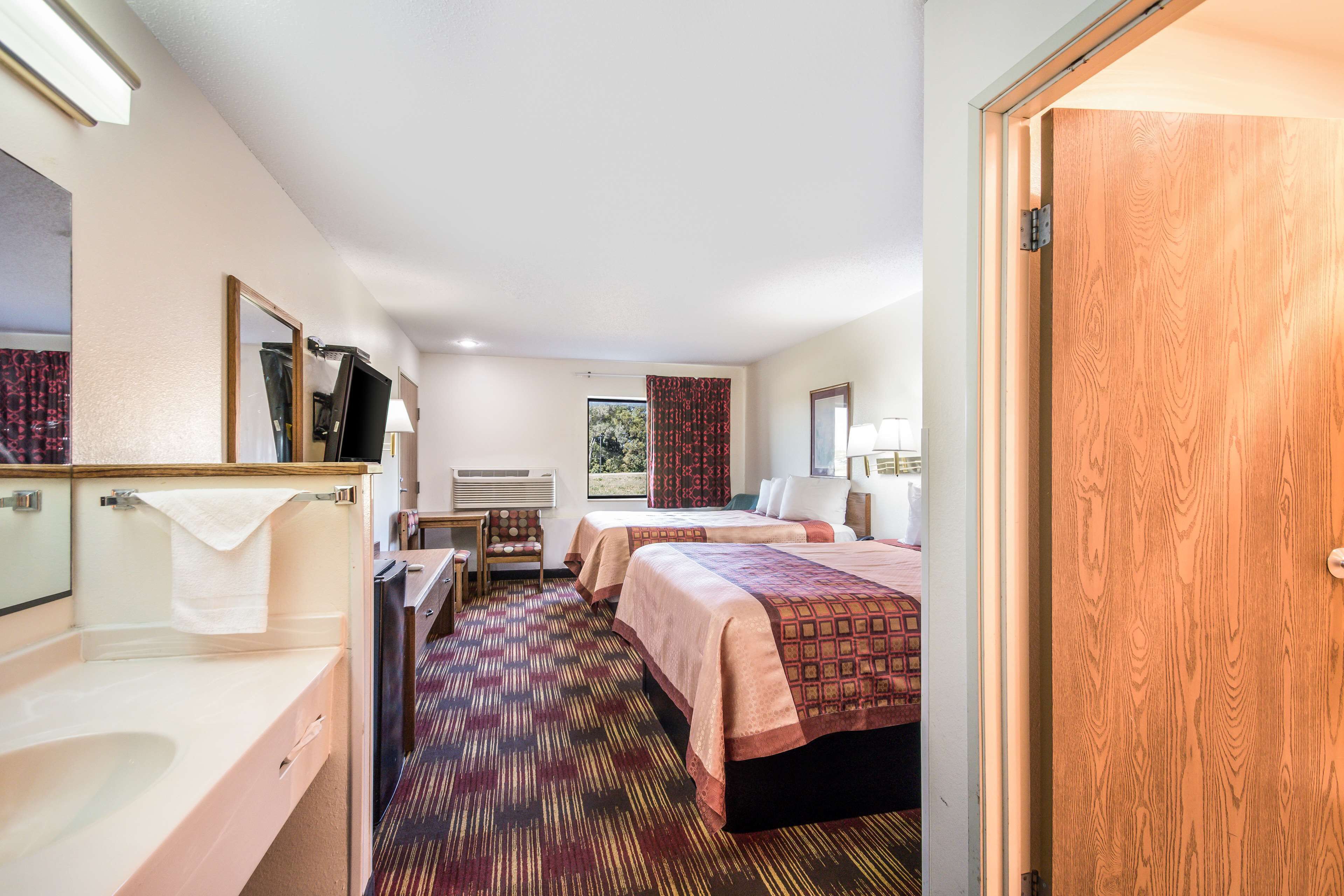 A hotel room with two beds, a bathroom with a sink and mirror, and a view of the outdoors.